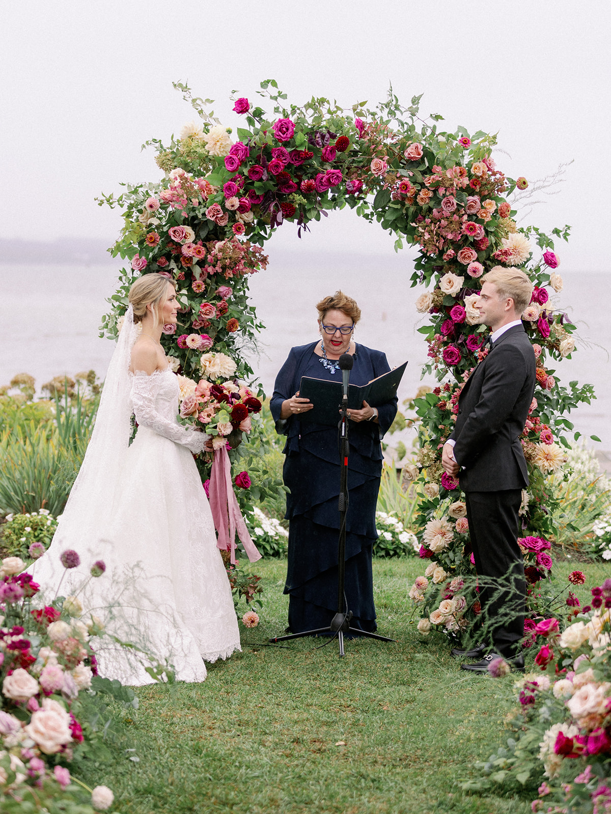 bride and groom at the flower arch getting married at the lake house 