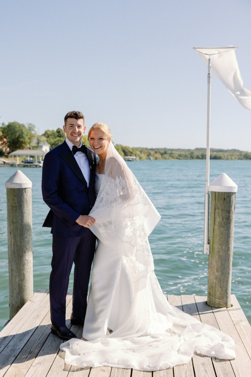 Bride and groom stand on dock overlooking the lake for wedding portraits.