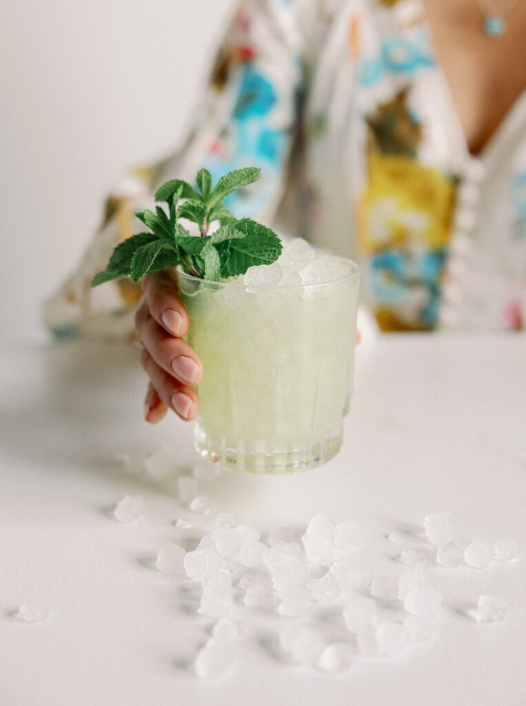 Wedding planner holding out a refreshing green cocktail as ice spills out on the table.