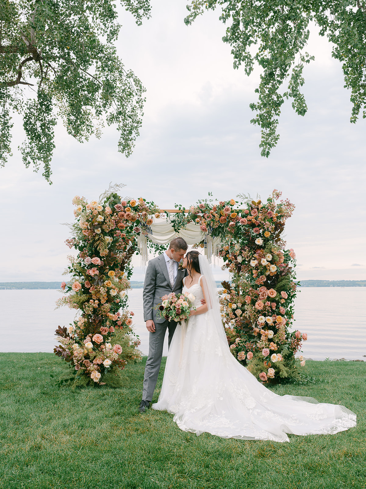 Bride and groom pose for portraits in front of floral arch after ceremony at Inns of Aurora.