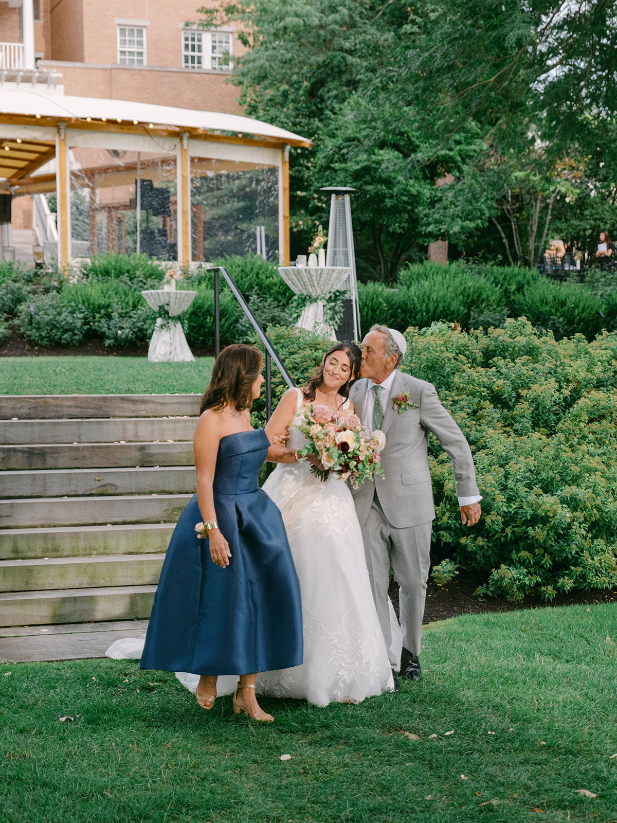Father kisses daughter as he and his wife walk their daughter down the aisle.
