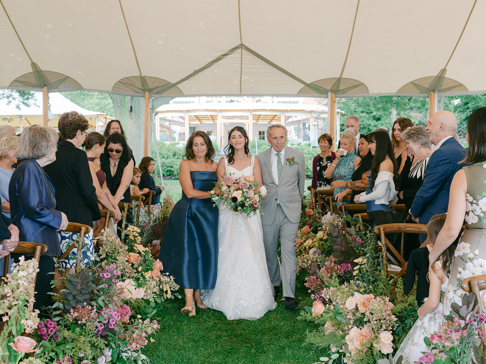 Mother and father walk their daughter down the aisle, surrounded by a beautiful fall wedding design.