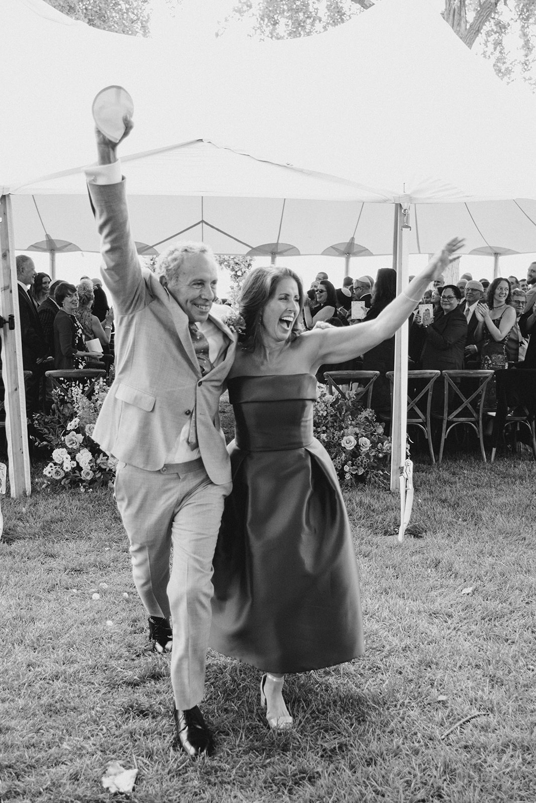 Mother and father of bride exit wedding ceremony as they cheer.