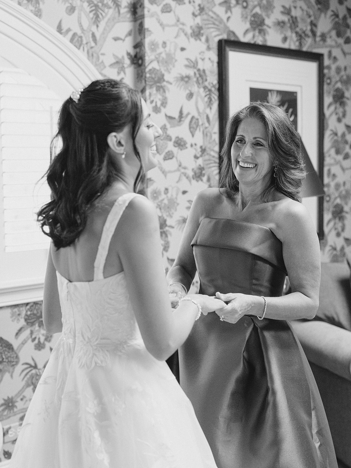 Mother and daughter laugh together as they hold hands and reminisce as they get ready for wedding day.