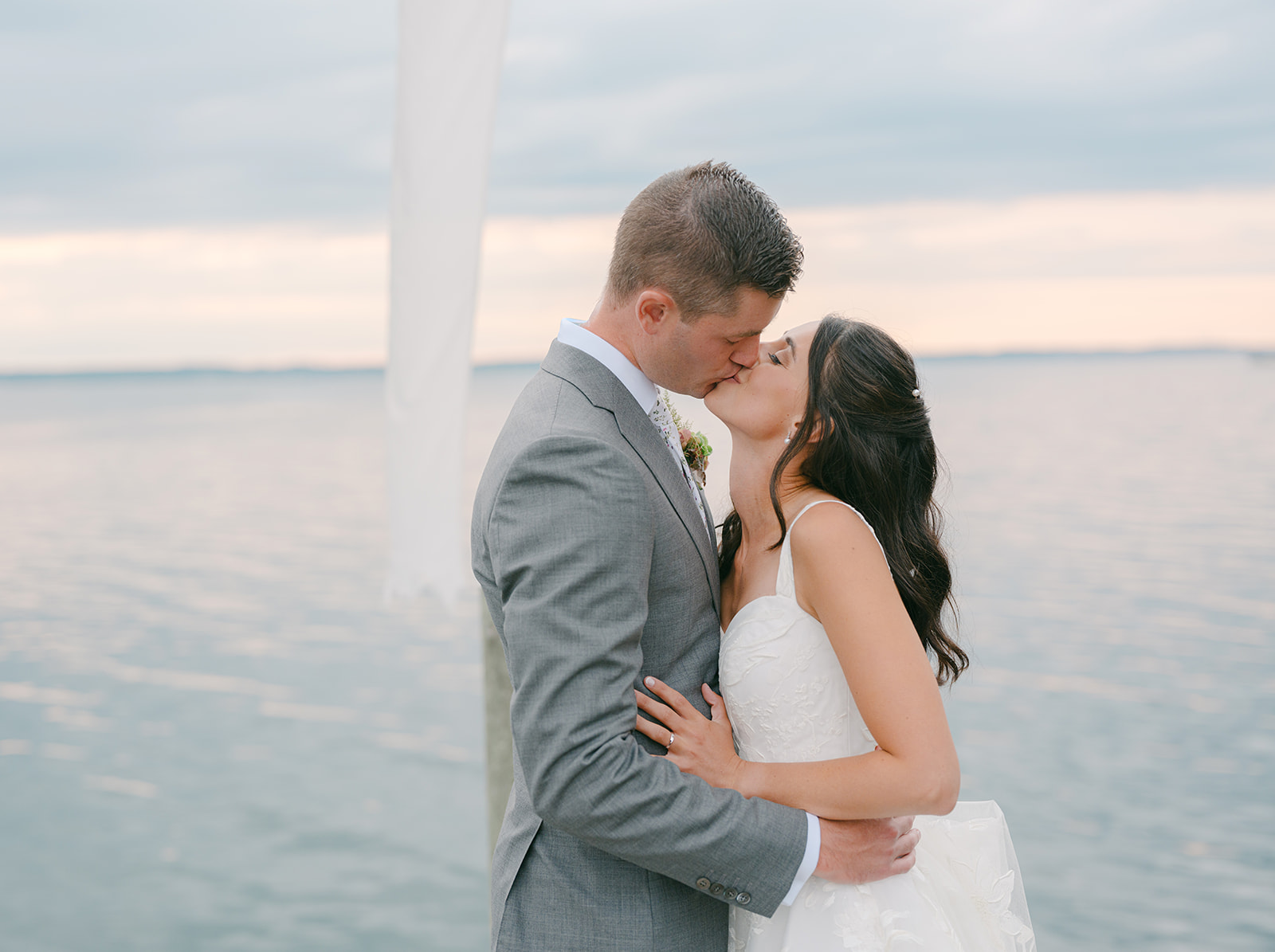 Bride and groom share kiss with a lake behind them.