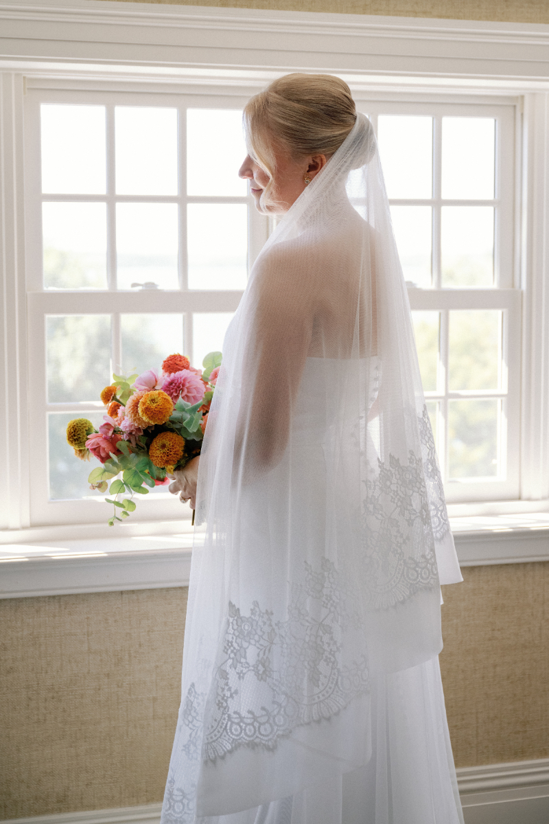 Bride stands facing window after she finished getting ready.