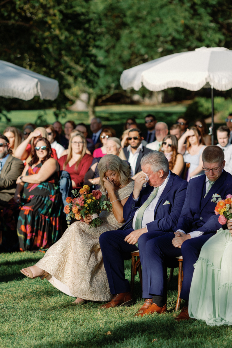Brides parents wipe tears during wedding ceremony as their daughter and son-in-law exchange vows.
