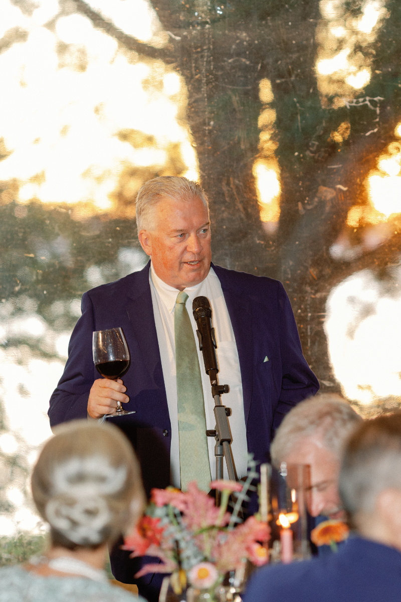 Father of the bride raises a glass as he finishes his toast during wedding reception.