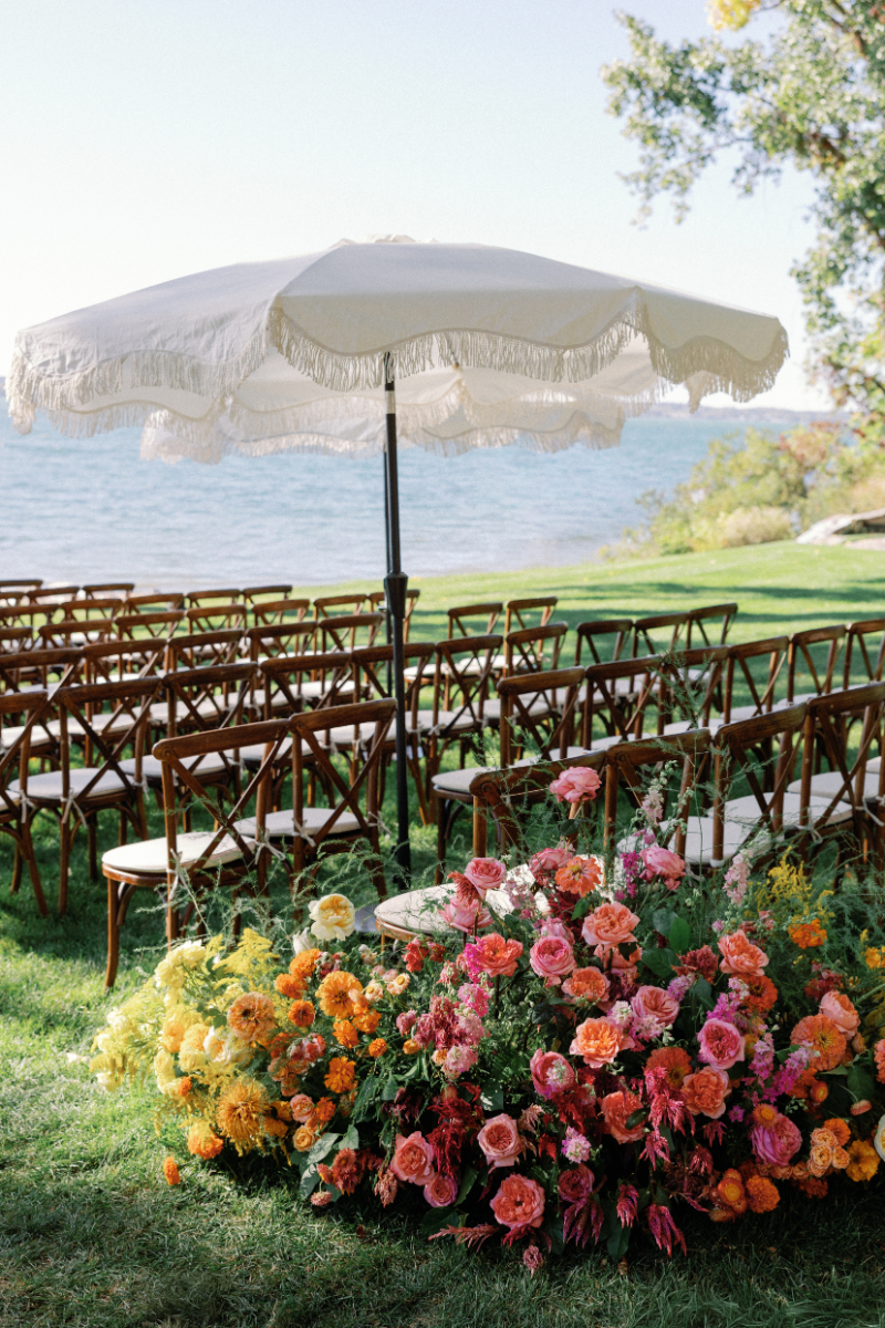 Ceremony setup at Inns of Aurora with wooden chairs, colorful aisle florals, and cream scalloped umbrellas.