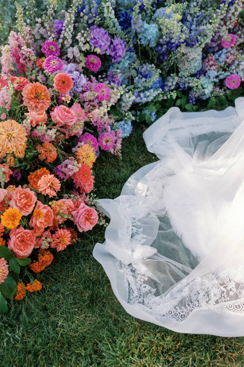 Close up details of colorful ceremony florals with the bride's dress train falling by them.