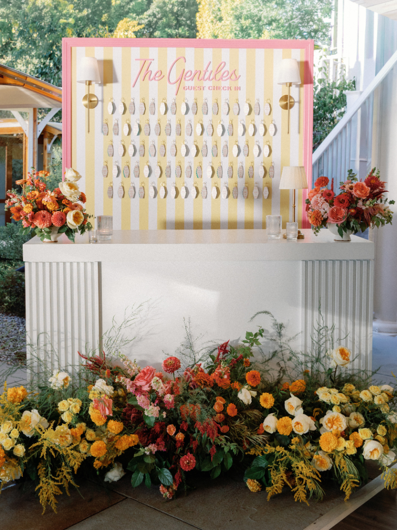 Custom Slim Aarons inspired wedding escort card table surrounded by colorful florals.