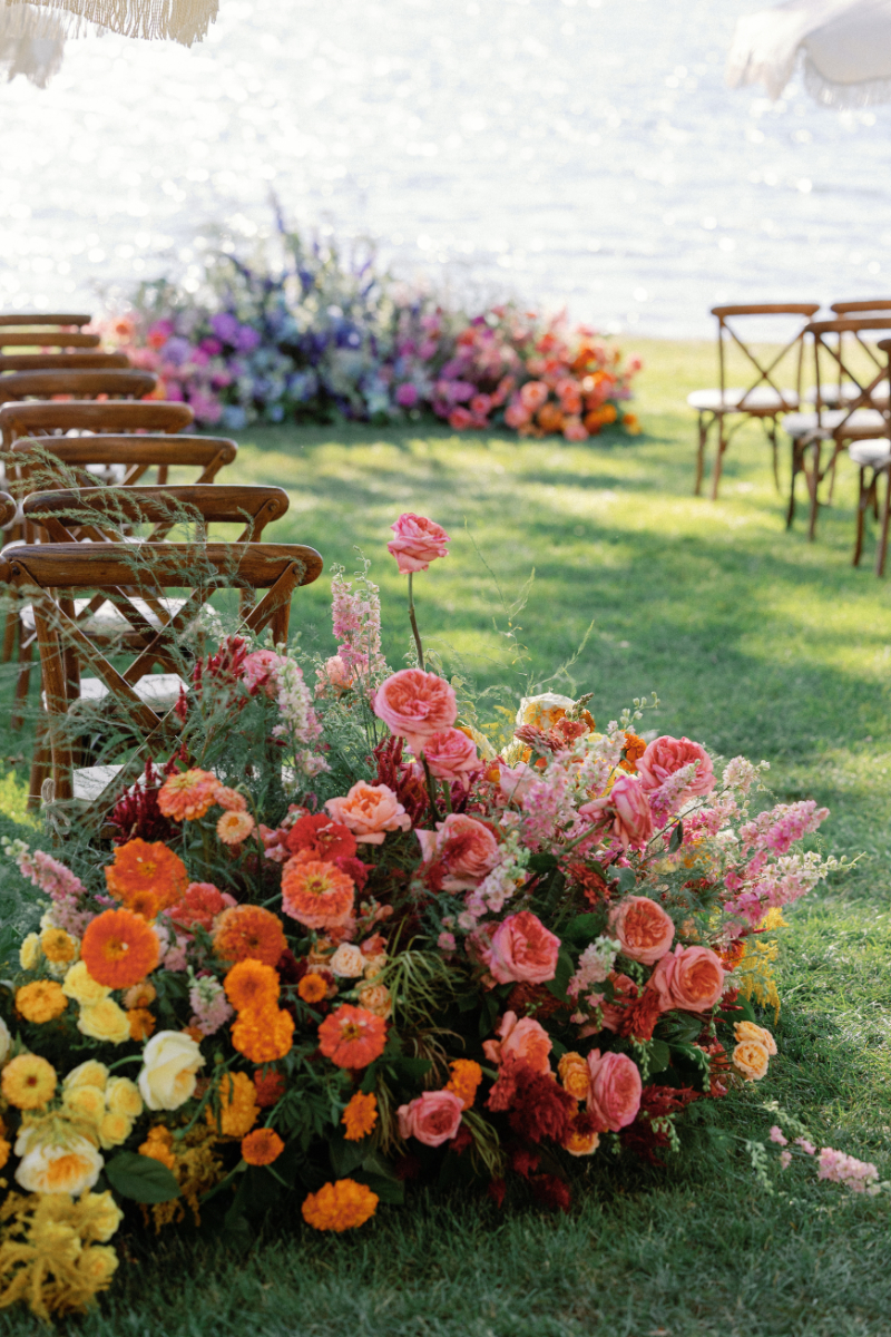 Colorful florals hug wooden ceremony chairs at the base of the aisle.