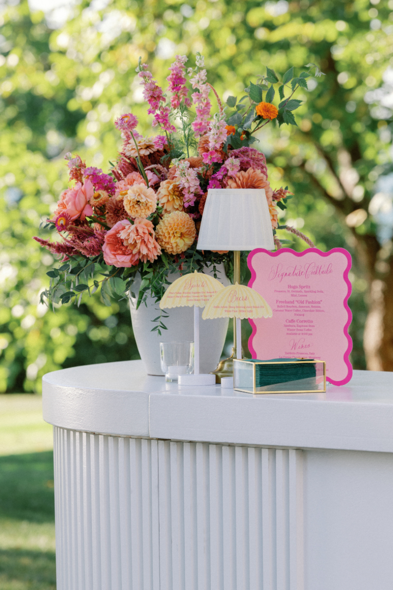 Bold, colorful floral arrangement next to custom signage for Slim Aarons inspired wedding cocktail hour.
