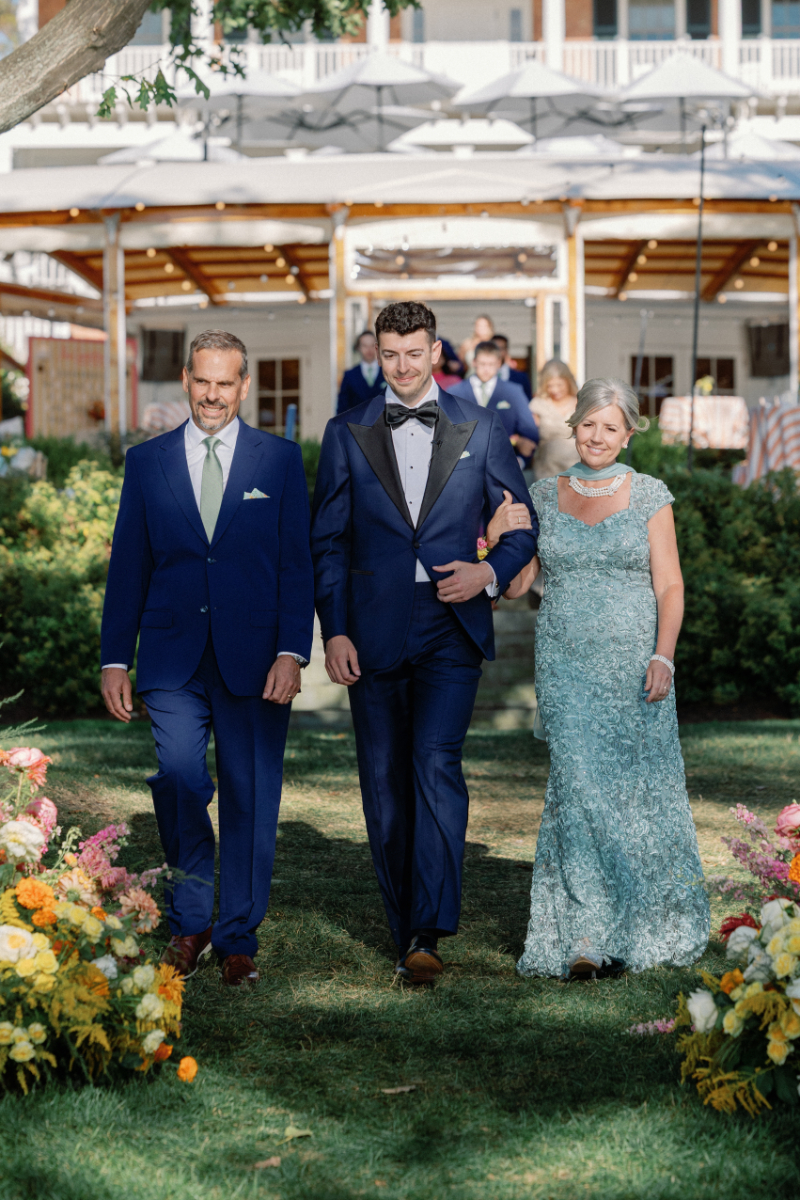 Groom walks down the aisle with his mother and father.