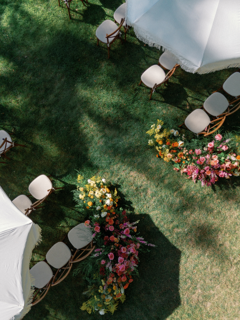 Aerial view of ceremony setup at Inns of Aurora, with wooden chairs, colorful aisle florals, and cream scalloped umbrellas.