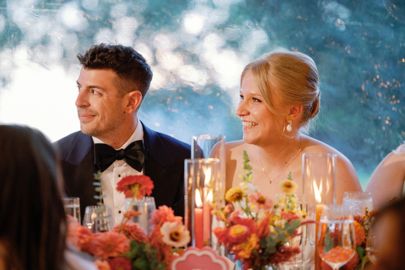 Bride and groom watch as guests give toasts.