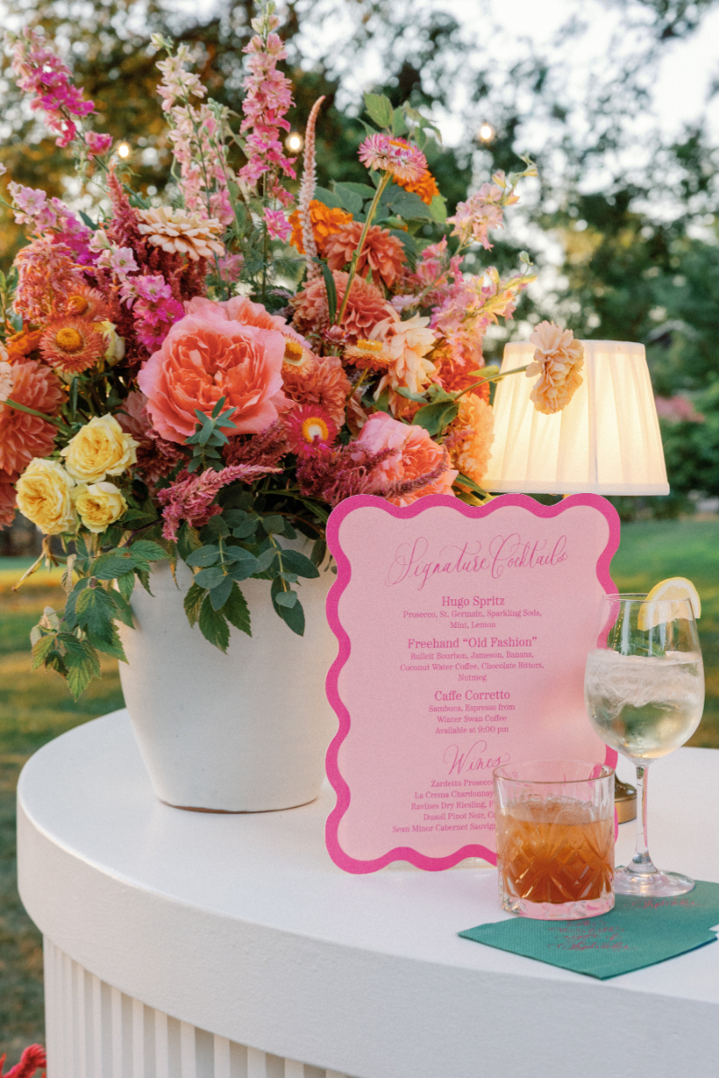 Signature cocktails in front of scalloped menu and large, colorful floral arrangement.