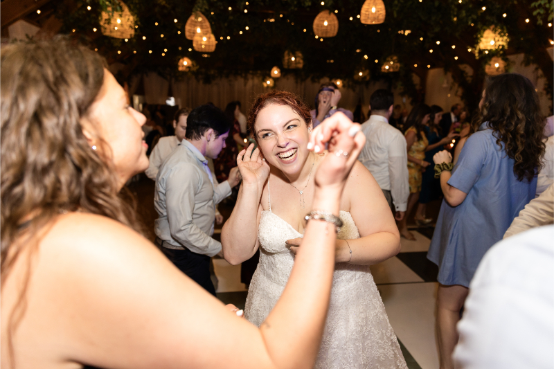 Bride smiles at friend as they dance together at wedding reception.