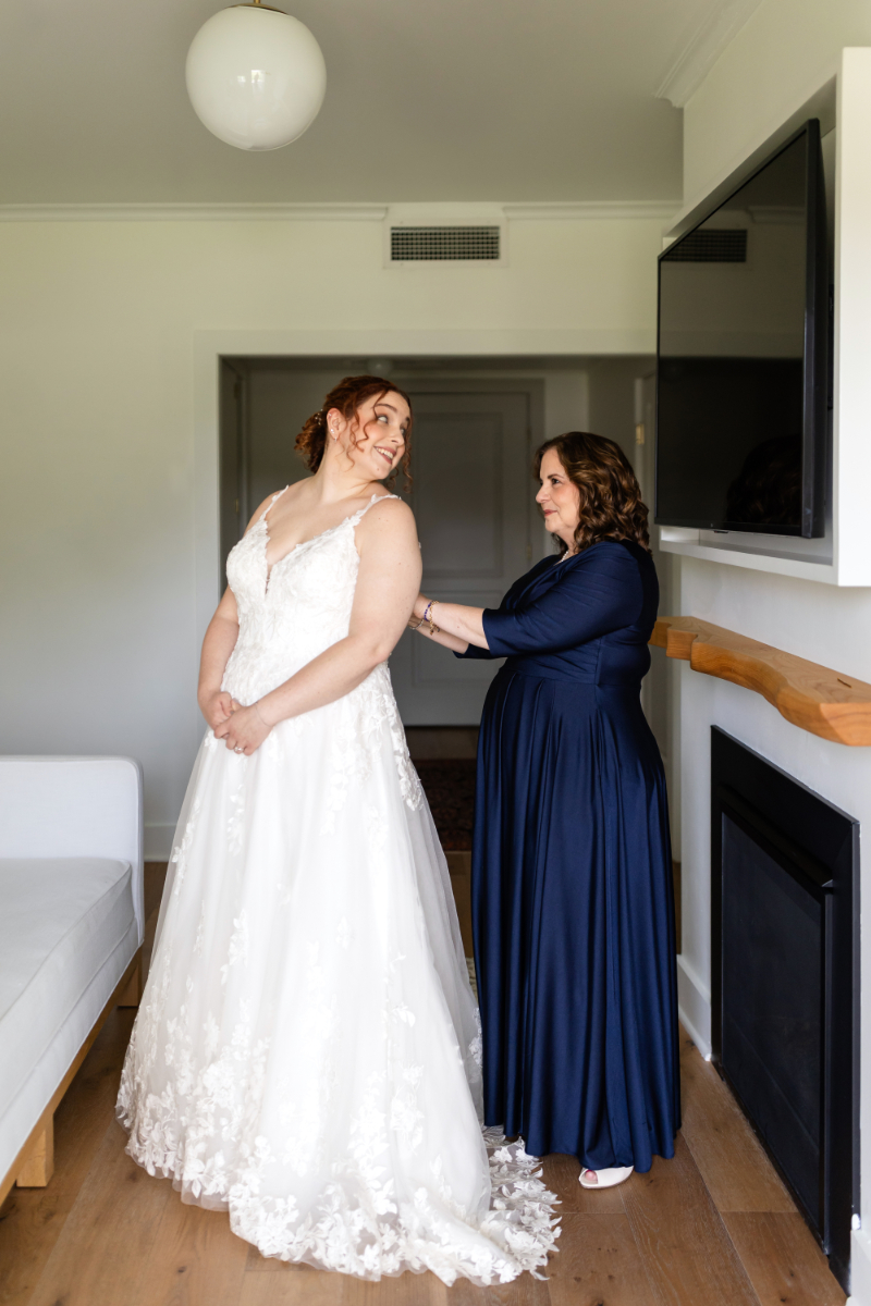 Bride looks back at her mom and she finishes getting her into her wedding dress.