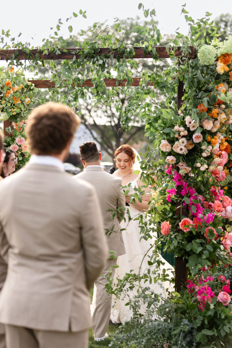 Bride and groom exchange vows under floral filled chuppah at The Lake House on Canandaigua.