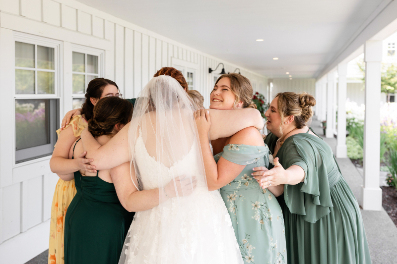 Bride and bridesmaids share hug after finishing getting ready for the day.