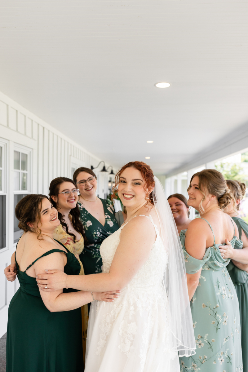 Bride turns around to face camera as her and bridesmaids share hug after getting ready.