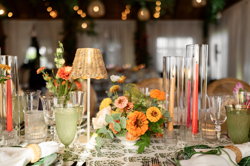 Table setting with color florals, taper candles in hurricanes, and mini rattan lamp.