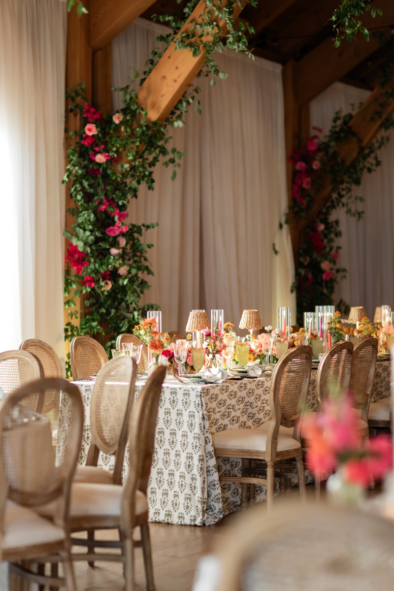Table setting with color florals, taper candles in hurricanes, and mini rattan lamps.
