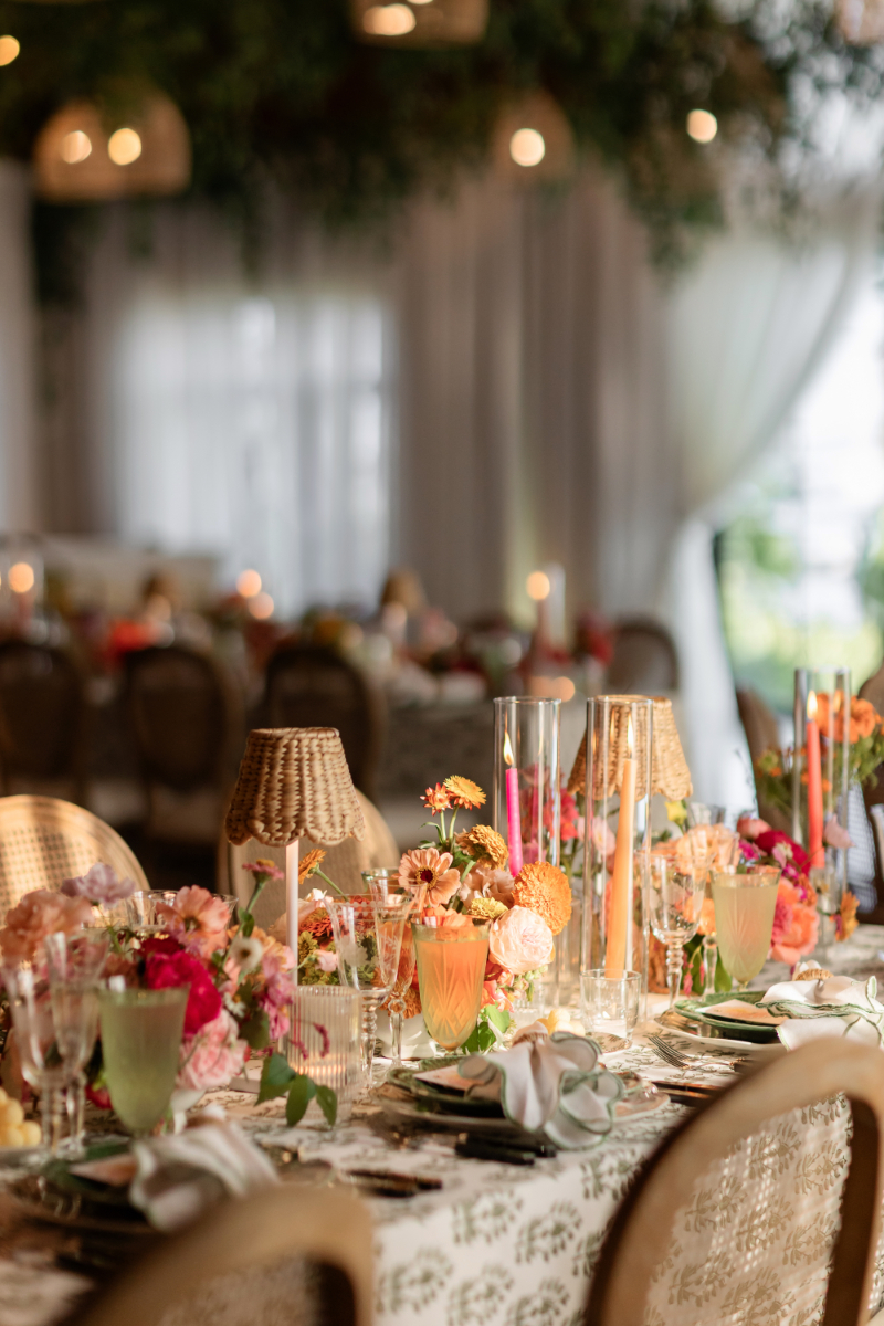 Table setting with color florals, taper candles in hurricanes, and mini rattan lamps.