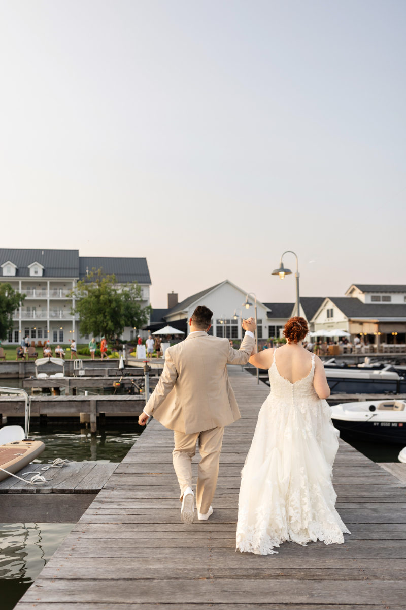 Bride and groom take pictures of as they walk on dock at their summer camp wedding at The Lake House on Canandaigua.