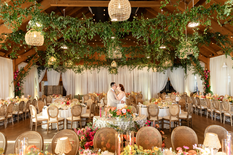 Bride and groom share kiss during private reception reveal, showcasing their dream summer camp wedding decor with bold colors and abundant florlas.