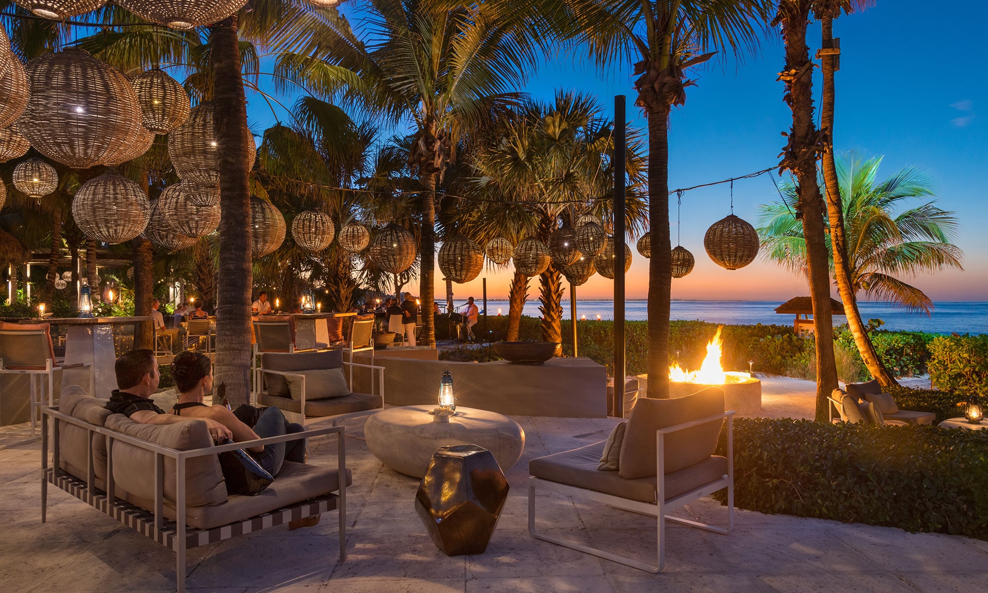 Couple sits near fire pit as the sun sets over the ocean at Grace Bay Club.