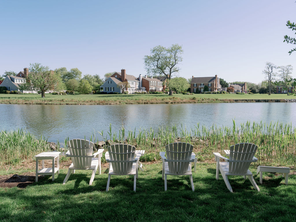 Four white Adirondack chairs sitting in grass in front of the river at Inn at Perry Cabin.
