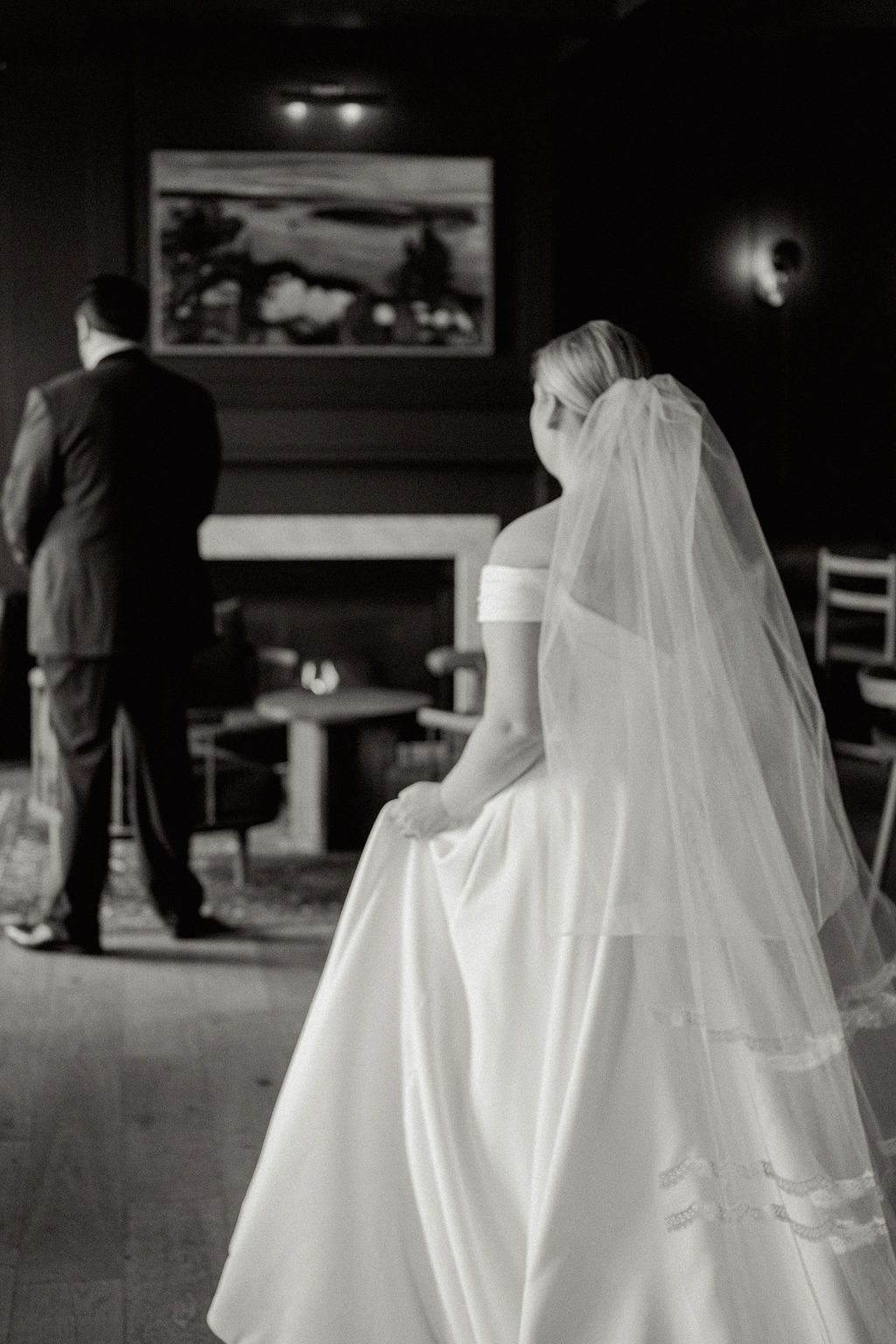 Black and white photo of bride walking up to groom from behind during their first look.