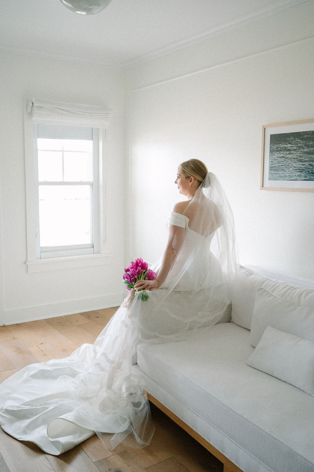 Bride sitting on edge of couch, looking to the side as she holds her tulip bouquet.