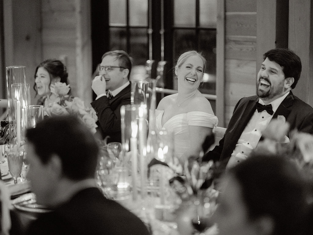 Bride and groom laughing as their family and friends share toasts.
