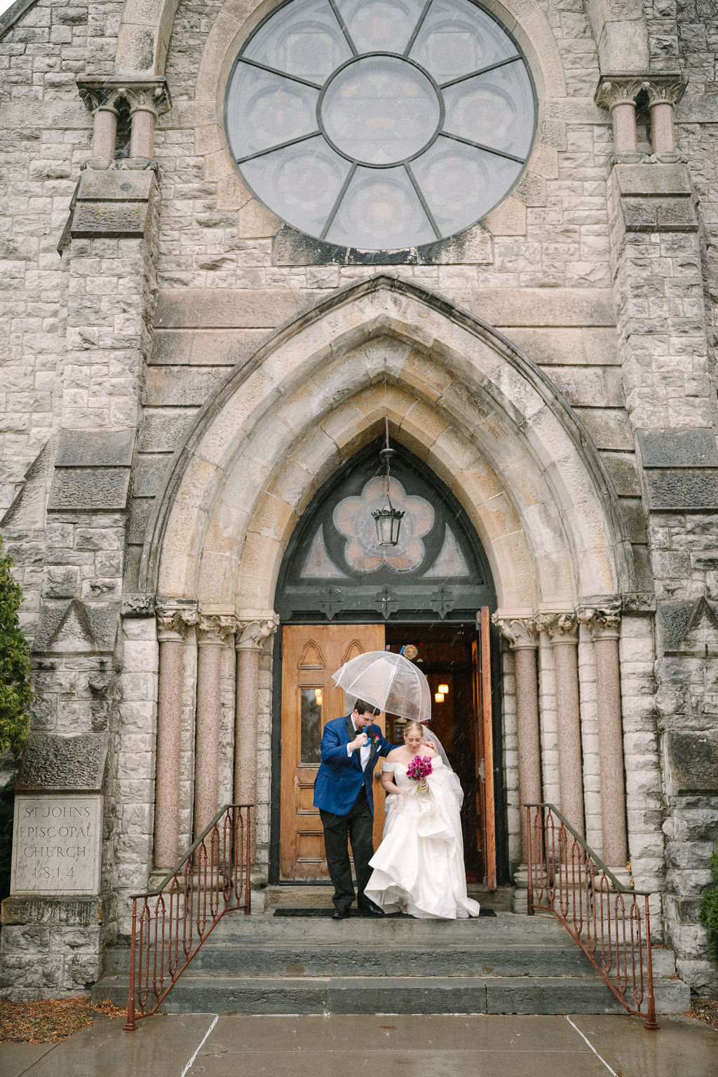 Groom holds umbrella over brides head as they leave their wedding ceremony.
