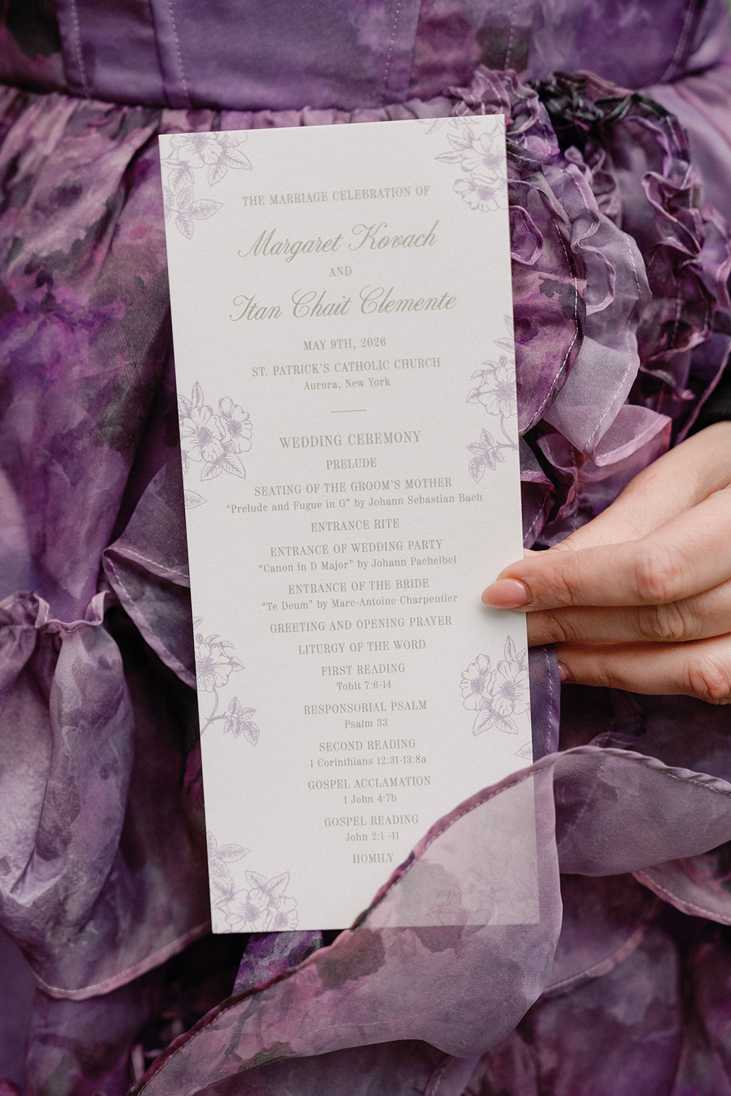 Close-up of a wedding ceremony program listing the order of service, held against a ruffled purple floral dress.