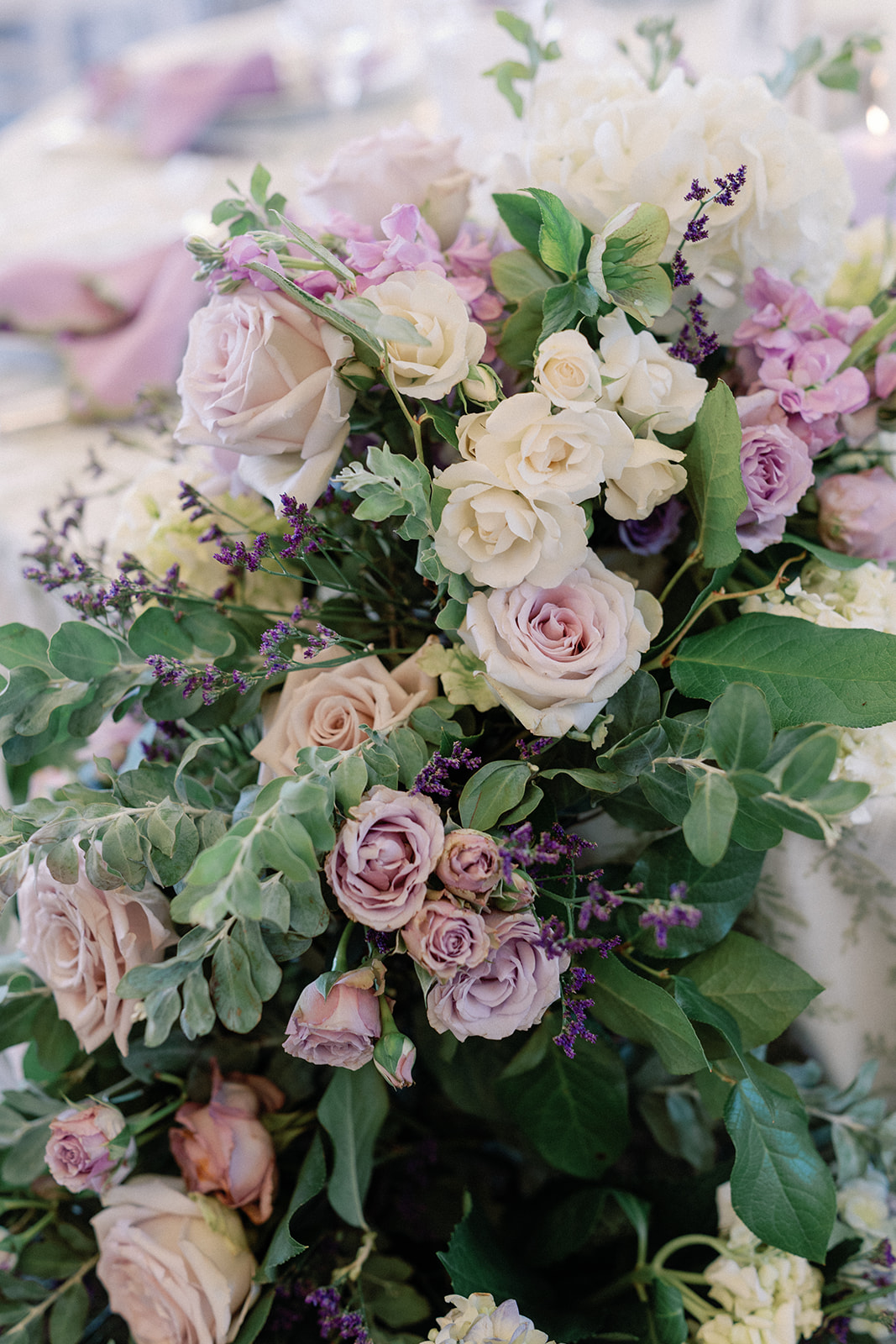 Close-up of a lush floral arrangement with blush, cream, and lavender roses, purple stock, and soft greenery.