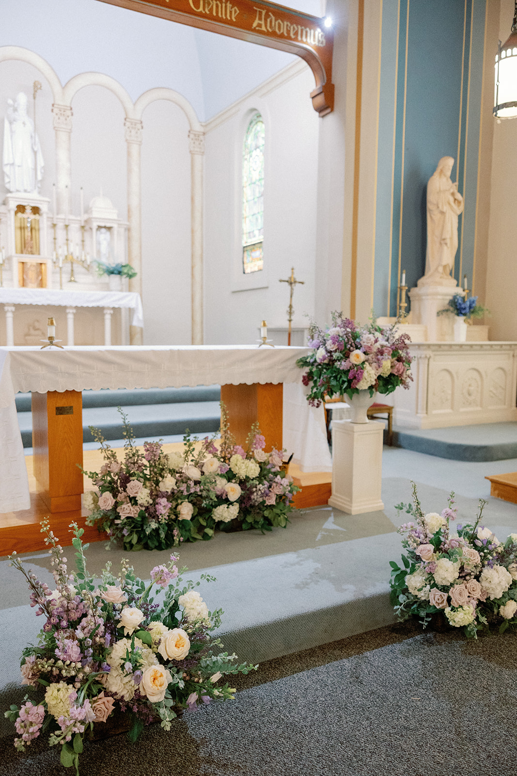 Close-up of the church altar with pastel floral arrangements in blush, lavender, and cream at its base, statues visible in the background.